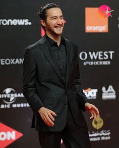 a man in a black suit and tie smiling at the camera on a red carpet