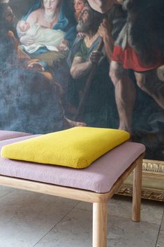 a bench with a yellow cushion on it in front of a painting