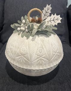 a white ceramic vase with holly and pine cones on it sitting on a black couch