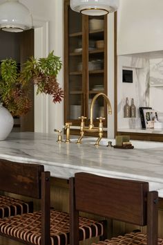 a kitchen with marble counter tops and gold faucet lights over the sink, surrounded by wicker chairs