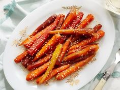 a white plate topped with carrots covered in sesame seeds and seasoning next to a fork