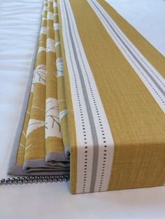 a close up of a bed with a white comforter and yellow striped bedspread