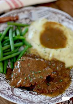 a plate topped with meat and gravy next to green beans