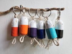 four different colored bottles hanging from a rope on a wall ornament with hooks