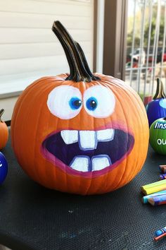 a pumpkin with an evil face painted on it and some crayons around it