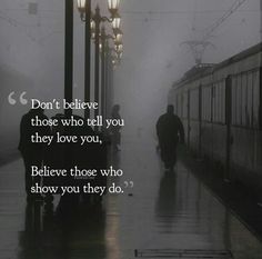 two people walking down a rain soaked street in front of a train with the words don't believe those who tell you they love you, believe