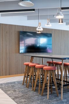 an office meeting room with wooden tables and orange stools in front of a flat screen tv