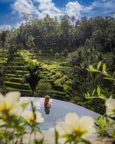 a woman sitting in the middle of a pool surrounded by lush green fields and trees