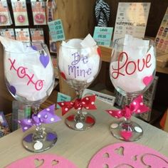 three wine glasses are decorated with pink and purple hearts on the table in front of a store