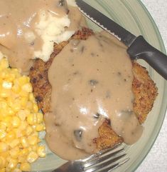 a plate with meat, mashed potatoes and gravy next to corn on the cob