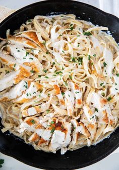 chicken alfredo in a skillet with parmesan cheese and herbs on the side