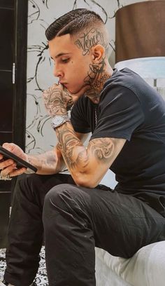 a man with tattoos sitting on a bed looking at his cell phone while holding it in his hand