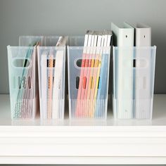 several clear plastic containers on a shelf with pens, pencils and file folders