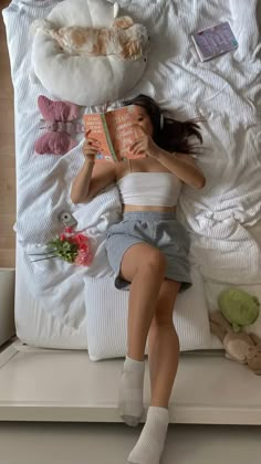 a woman laying in bed reading a book with stuffed animals on the pillow behind her