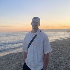 a man standing on top of a sandy beach next to the ocean at sun set