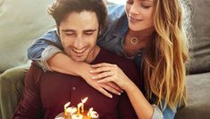 a man and woman sitting next to each other in front of a cake with candles on it