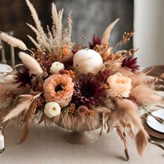 a vase filled with lots of flowers and feathers on top of a dining room table