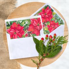 two envelopes decorated with poinsettias and greenery on a wooden table