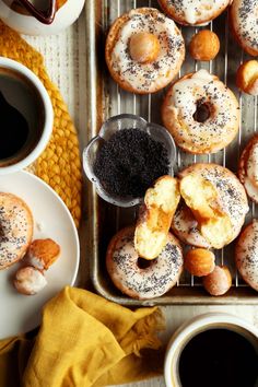 there are many doughnuts on the tray next to cups of coffee and saucers