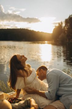 a man and woman sitting next to each other on a blanket near the water at sunset