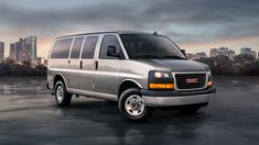 a silver van is parked in an empty parking lot with the city skyline behind it