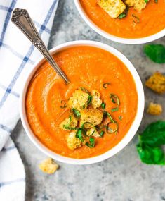 two bowls of tomato soup with bread croutons on the side and a spoon in one bowl