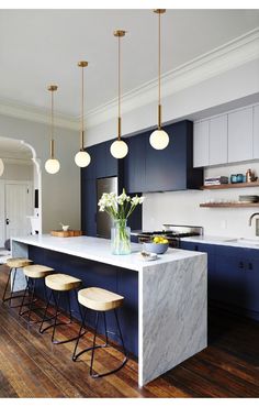 a kitchen with blue cabinets and marble counter tops, stools at the center island