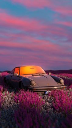 a car is parked in the middle of a field with purple flowers on it at sunset