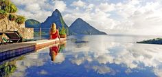 a woman sitting on the edge of a swimming pool looking out at mountains and water