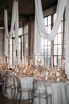 the tables are covered with white tablecloths and gold candles in front of large windows