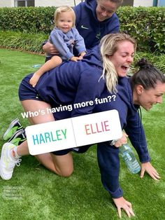 two women and a child are playing on the grass with a sign that says, who's having more fun?