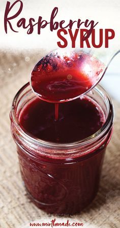 a spoon full of raspberry syrup sitting on top of a jar filled with jam