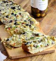 two slices of bread with olives and cheese on a cutting board next to a bottle of wine