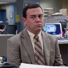 a man in a suit and tie sitting at a desk with a computer monitor behind him