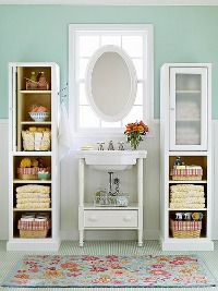 a white sink sitting next to a bathroom mirror on top of a cabinet filled with towels