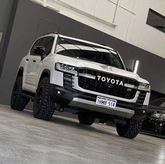 a white truck parked in front of a gray building with two other trucks behind it