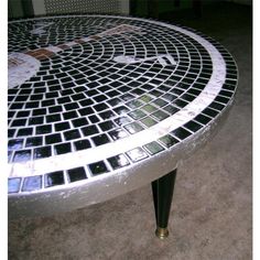 a metal table with black and white tiles on it's top, sitting in a room