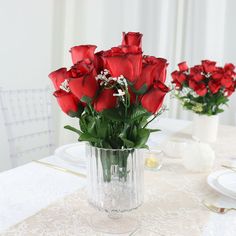 a vase filled with red roses sitting on top of a white tablecloth covered table