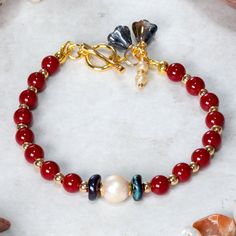 Beautiful Red coral, Pearl and gold plated Hematite bracelet designed and handcrafted with care and attention to detail. The bracelet is  hand threaded onto quality 19 strand beading wire for flexibility and durability using:     6mm dyed Red Coral beads,     Freshwater pearl focal bead,     2mm Gold plated Hematite beads,      Dark blue wavy Picasso Czech glass accent disc     beads.  The bracelet measures 19cm and is fastened using a quality 18ct gold plated toggle clasp which is adorned with Adjustable Red Jewelry With Pearl Charm, Elegant Red Handmade Charm Bracelet, Elegant Handmade Red Charm Bracelet, Red Pearl Bracelets With Round Beads, Red Pearl Beaded Bracelets As Gift, Hand-strung Red Pearl Beaded Bracelets As Gifts, Handmade Red Pearl Bracelet With Round Beads, Red Pearl Bracelets As A Gift, Red Pearl Bracelets For Gifts