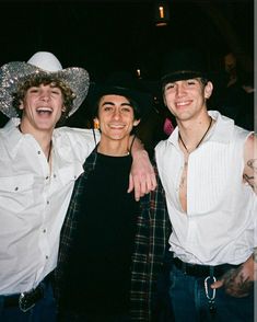 three young men standing next to each other in front of a crowd wearing cowboy hats