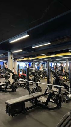 a gym with rows of weight machines and people working in the background at night time