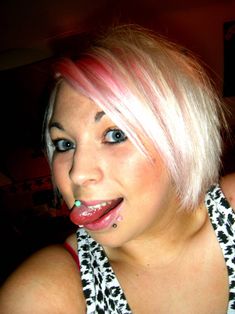 a woman with pink hair and piercings on her tongue is making a face to the camera