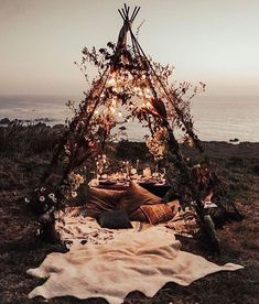 a teepee is set up with lights and blankets on the grass near the ocean