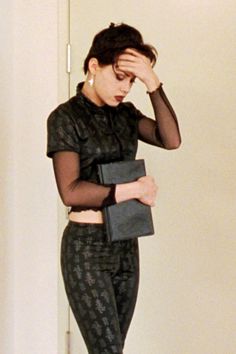 a woman in black is holding her hand on her head while standing next to a white wall