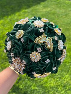 a bridal bouquet with brooches and flowers in the shape of butterflies is held by a woman's hand