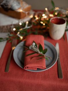 a place setting with napkins, silverware and greenery on the table top