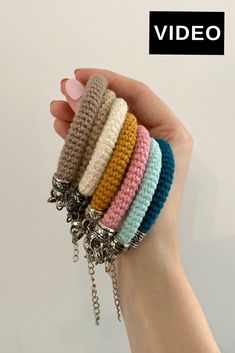 a hand holding a bunch of multi colored crochet bracelets with chains attached to them