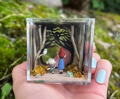 a person holding up a small glass block with an image of two gnomes in the woods