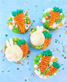 four cupcakes decorated with carrots, grass and sprinkles on a blue surface