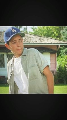 a young boy wearing a baseball cap standing in front of a house and looking at the camera